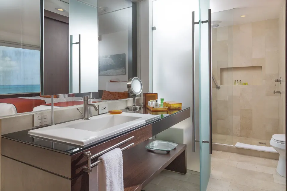 Guest bathroom with glass shower and ocean reflection at InterContinental Presidente Cancun Resort.