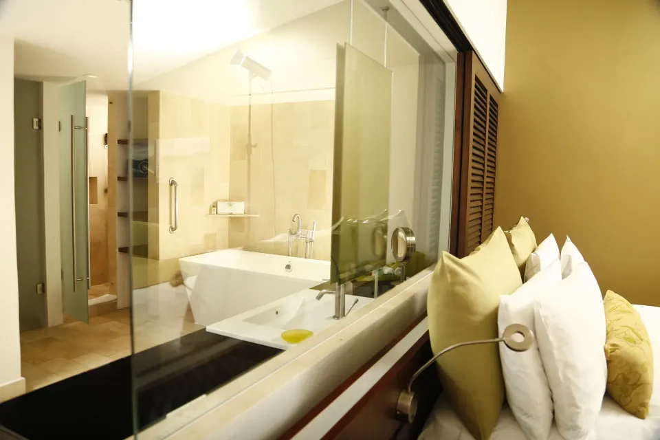 Glass-walled bathroom beside a guest bed at InterContinental Presidente Cancun Resort.