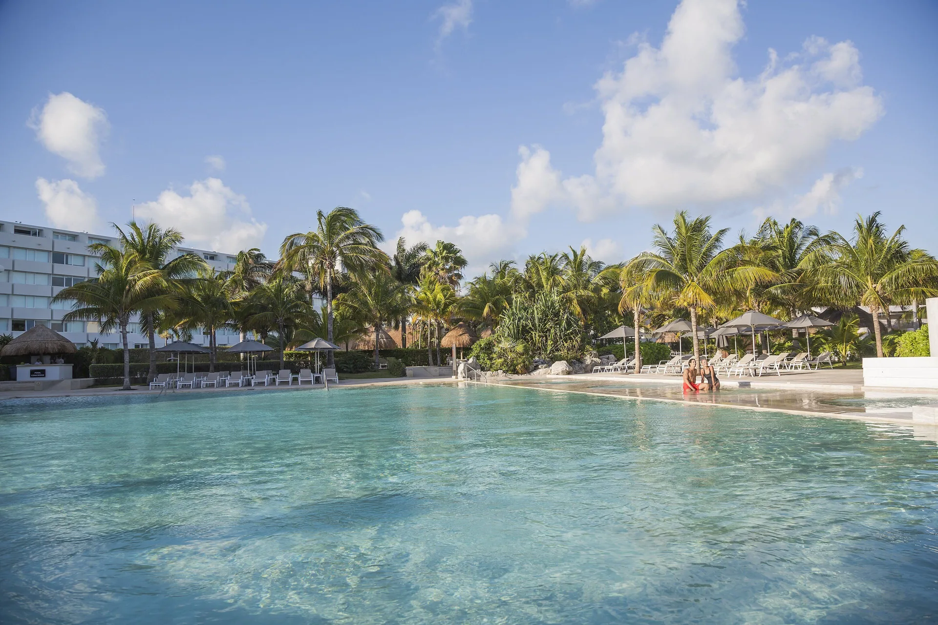 Large resort pool with palm trees and loungers at InterContinental Presidente Cancun Resort.