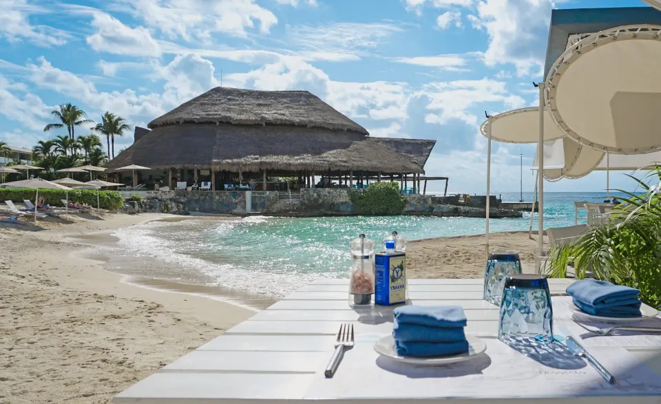 Table set on the sand with palapa restaurant in background at InterContinental Presidente Cozumel Resort Spa