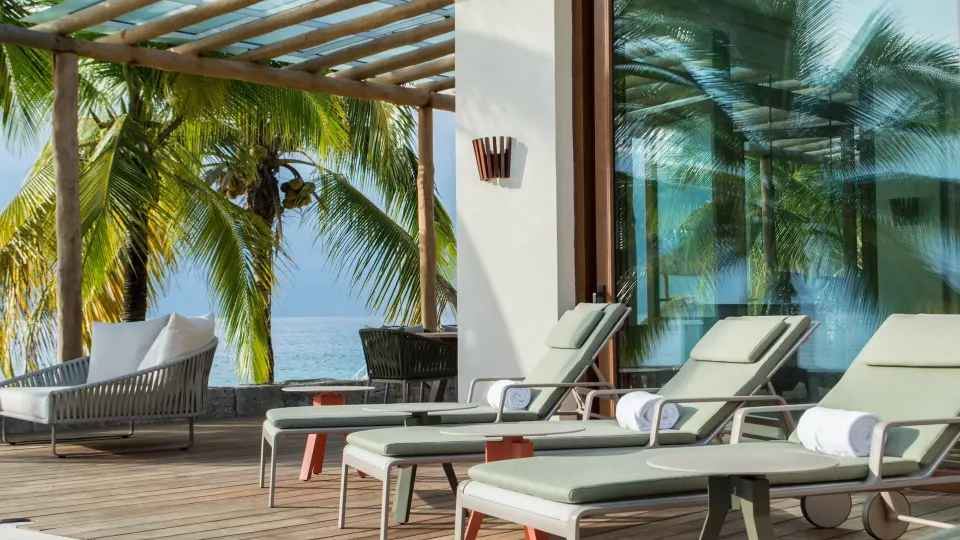 Outdoor lounge chairs and shaded seating by palm trees at InterContinental Presidente Cozumel Resort Spa