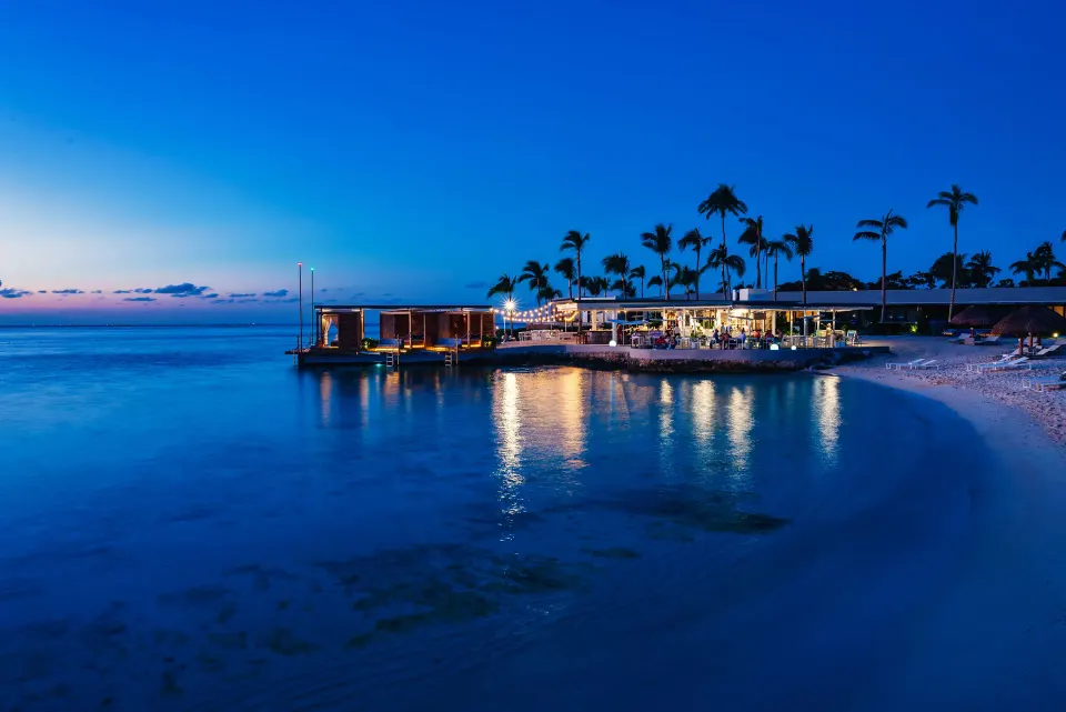 Evening view of resort shoreline with lit beach bar and palm trees at InterContinental Presidente Cozumel Resort Spa