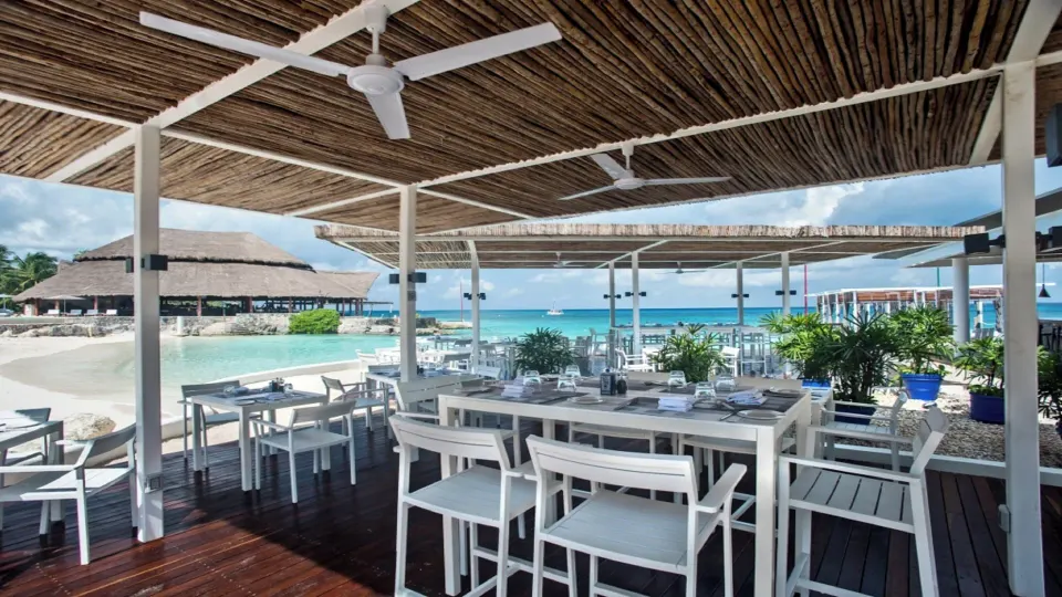 Covered oceanfront dining deck with white chairs and view of palapa at InterContinental Presidente Cozumel Resort Spa