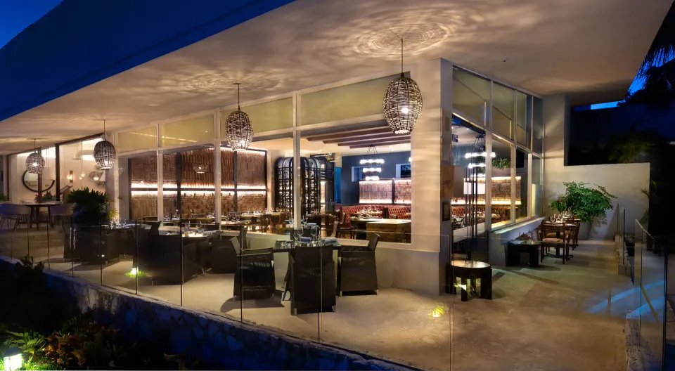 Evening view of an indoor glass-walled restaurant with tables and soft lighting at InterContinental Presidente Cozumel Resort