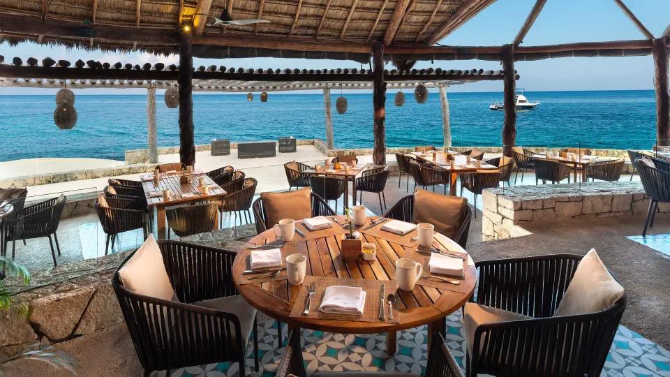 Thatched-roof seaside dining with round tables overlooking the ocean at InterContinental Presidente Cozumel Resort Spa