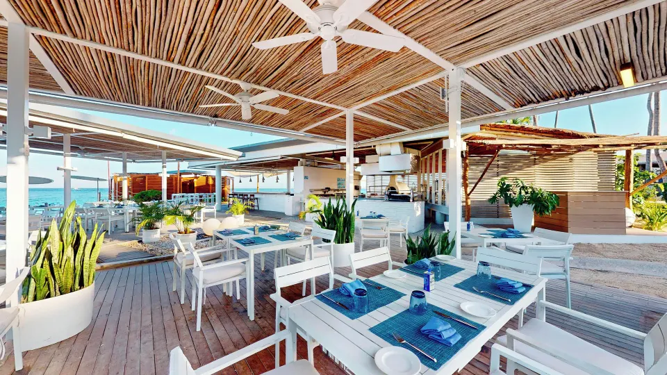 Shaded beachfront dining area with white tables and blue place settings at InterContinental Presidente Cozumel Resort Spa