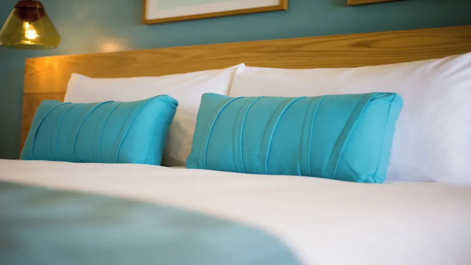 Close-up of turquoise bolster pillows on a made bed in a Classic Room at InterContinental Presidente Cozumel Resort Spa