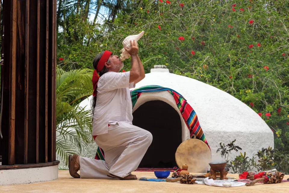 Ceremonial participant blowing a conch shell in front of a small domed structure at InterContinental Presidente Cozumel Resor