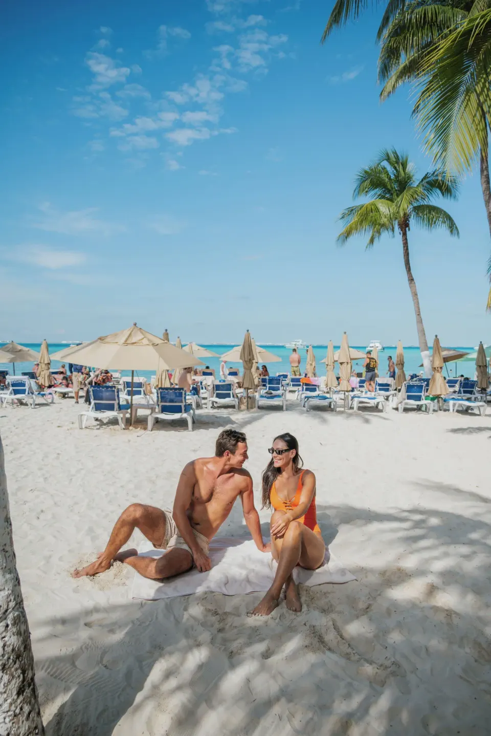 Couple sits on a towel beneath palms on the beach at Ixchel Beach Hotel.