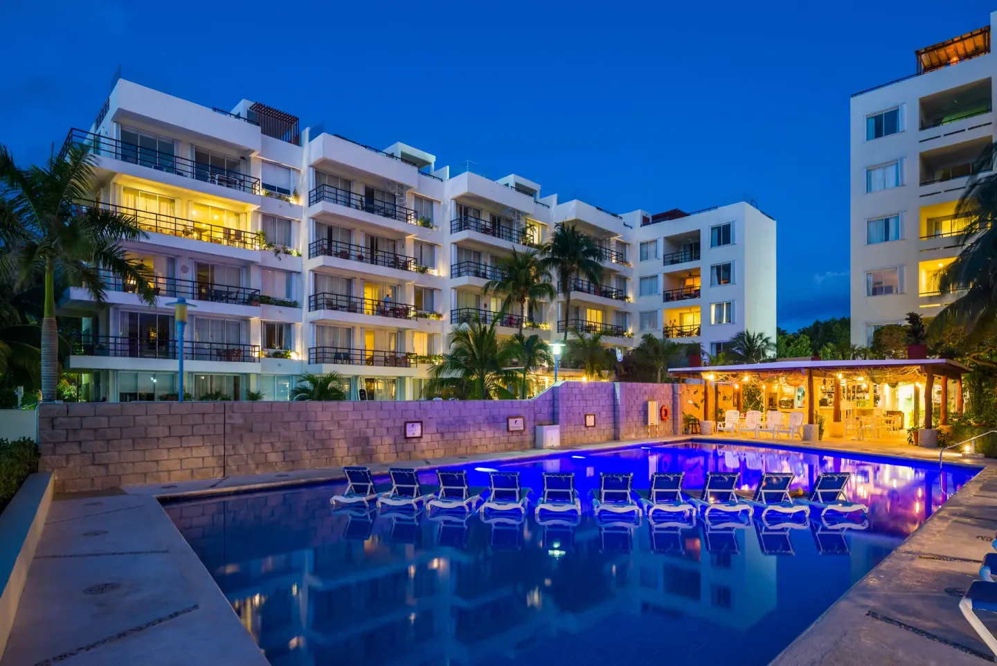 Evening pool scene with lit resort buildings at Ixchel Beach Hotel.