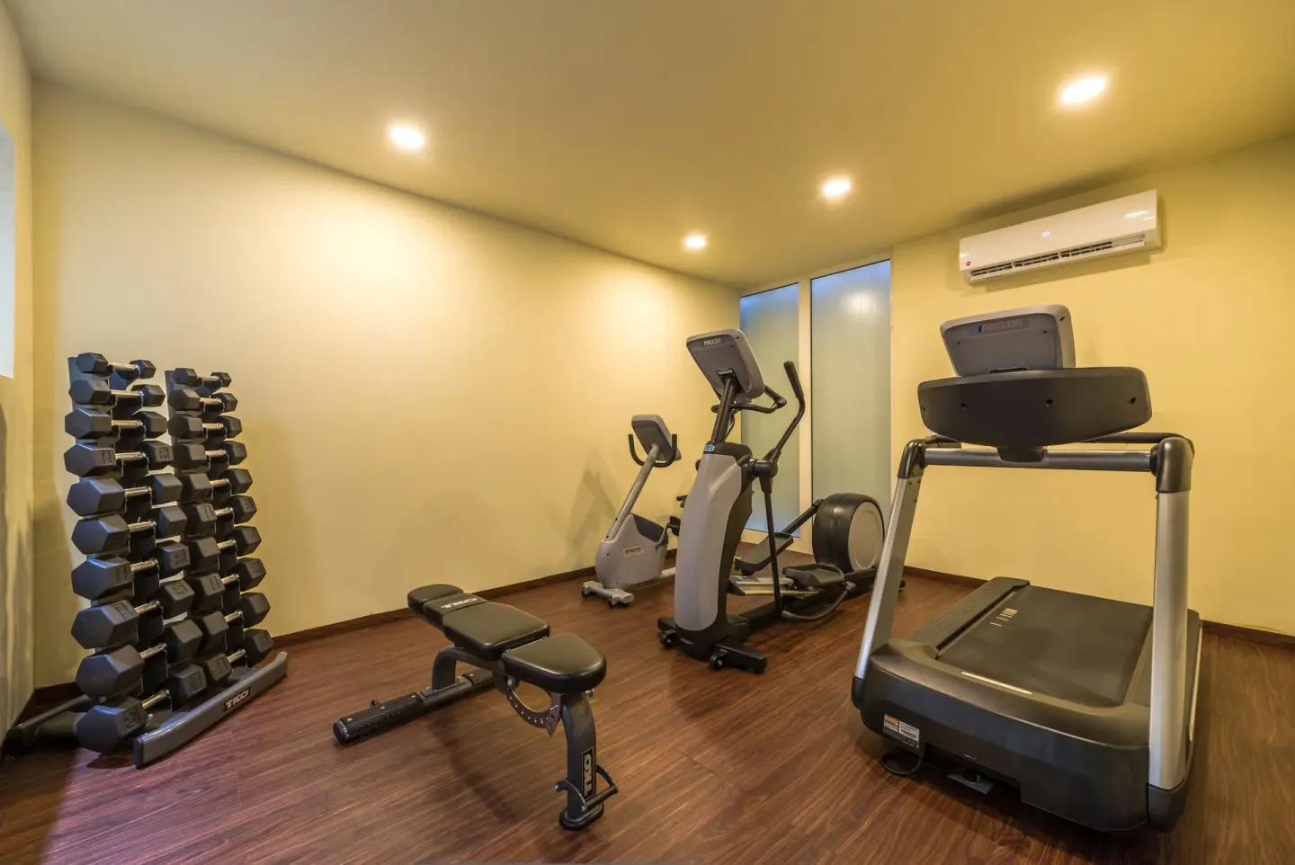 A treadmill, bench, dumbbell rack, and cardio machines are shown at Ixchel Beach Hotel.
