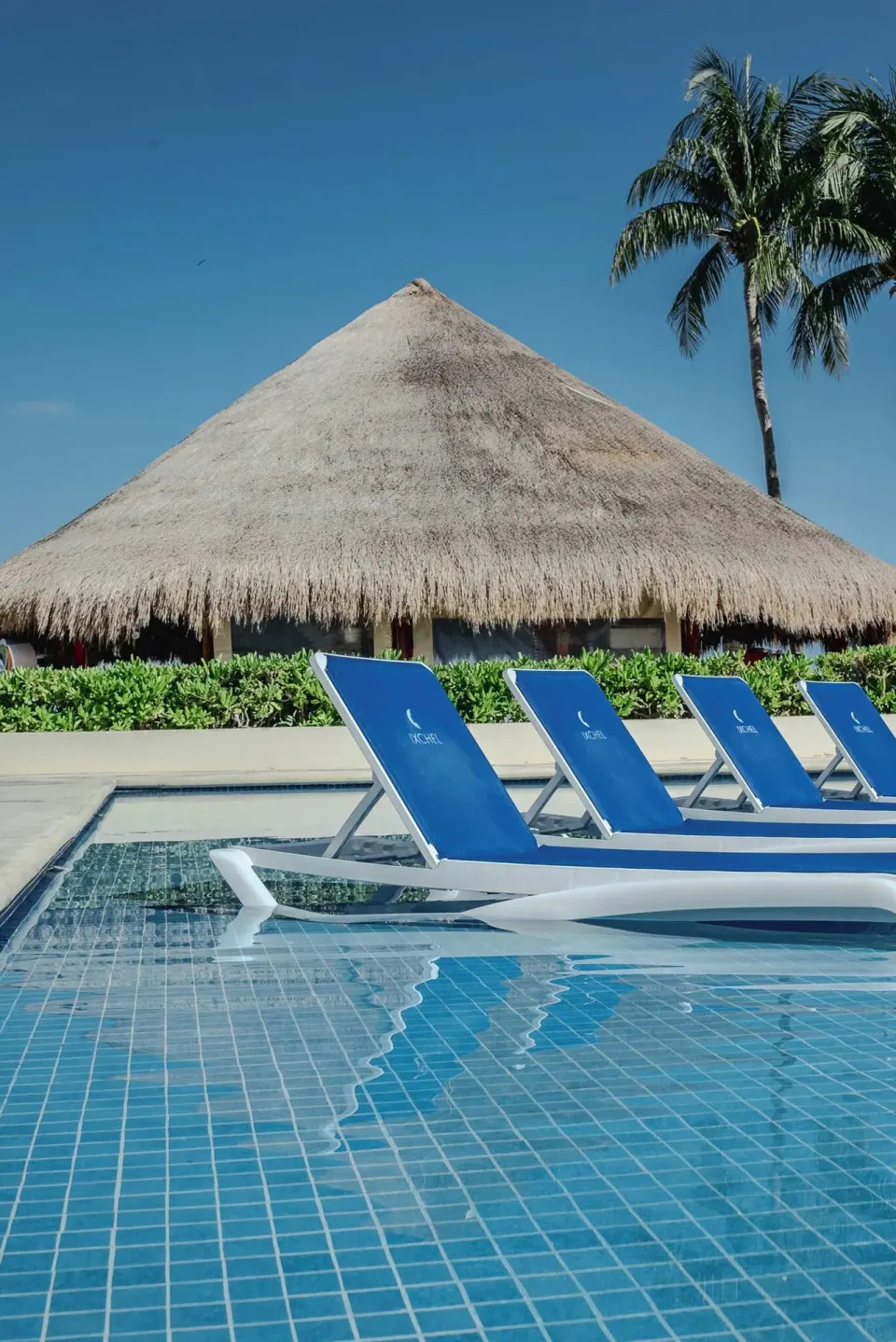 Blue pool loungers sit beside a thatched palapa at Ixchel Beach Hotel.