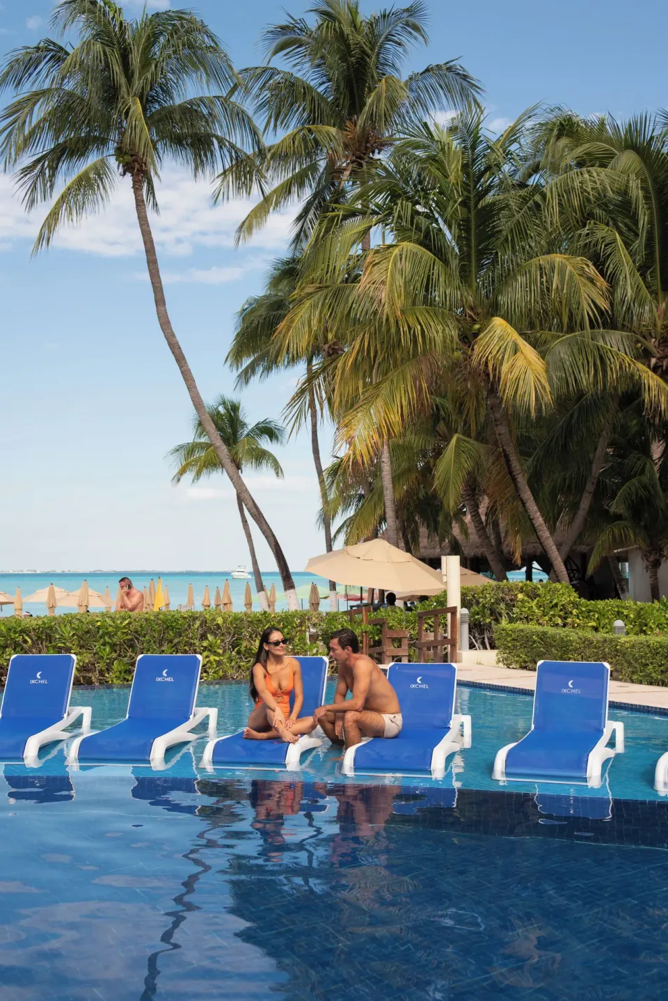 Guests sit on blue pool loungers near palm trees at Ixchel Beach Hotel.