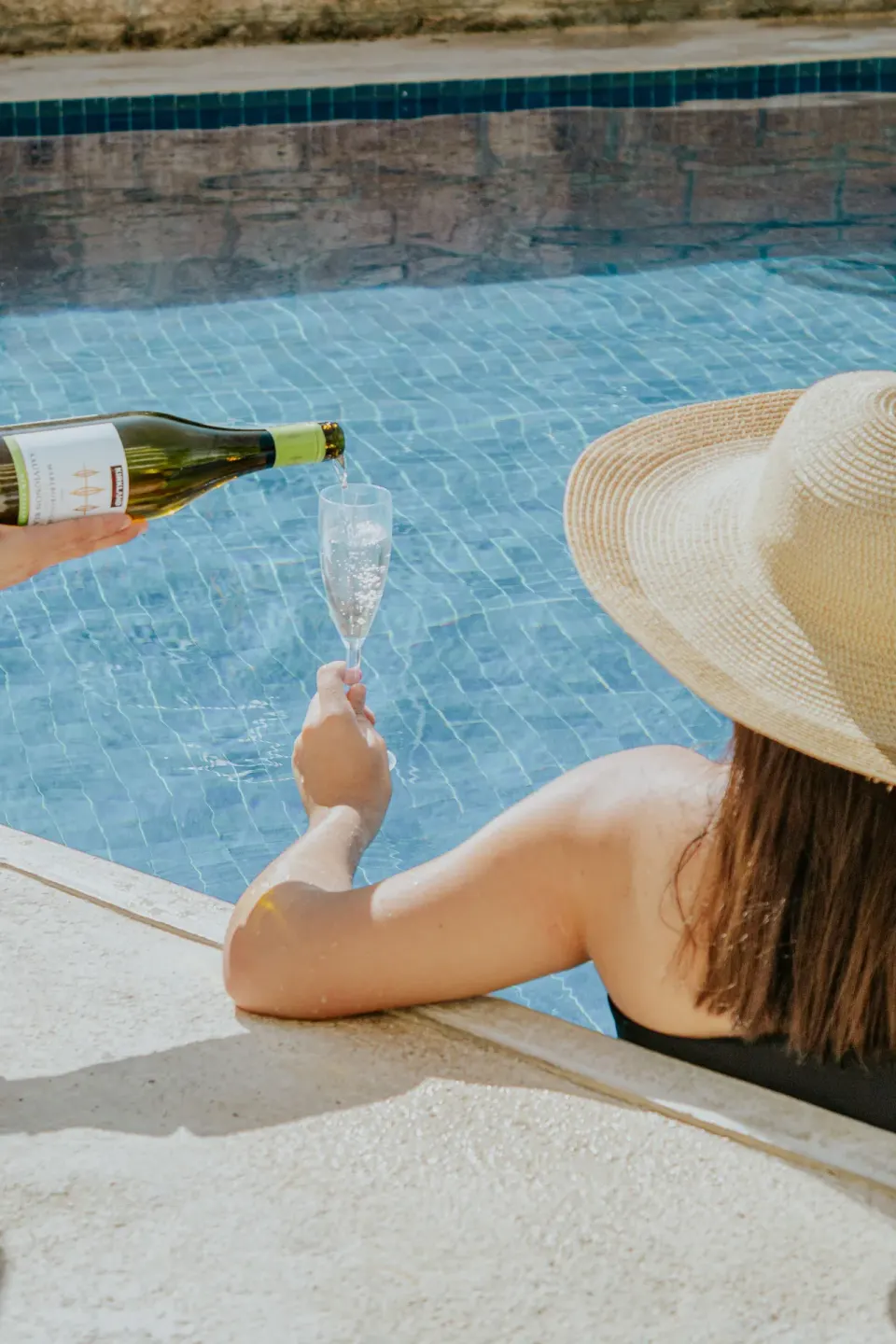 Guest in a sun hat receives a pour of sparkling wine by the pool at Ixchel Beach Hotel.