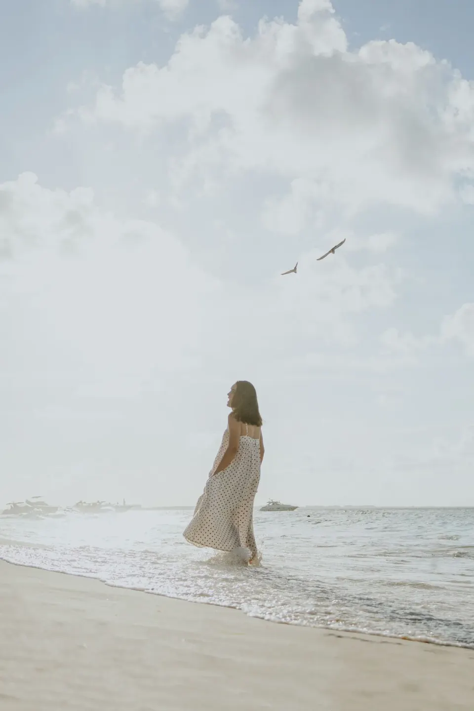 Woman walks through shallow surf under a cloudy sky near Ixchel Beach Hotel.