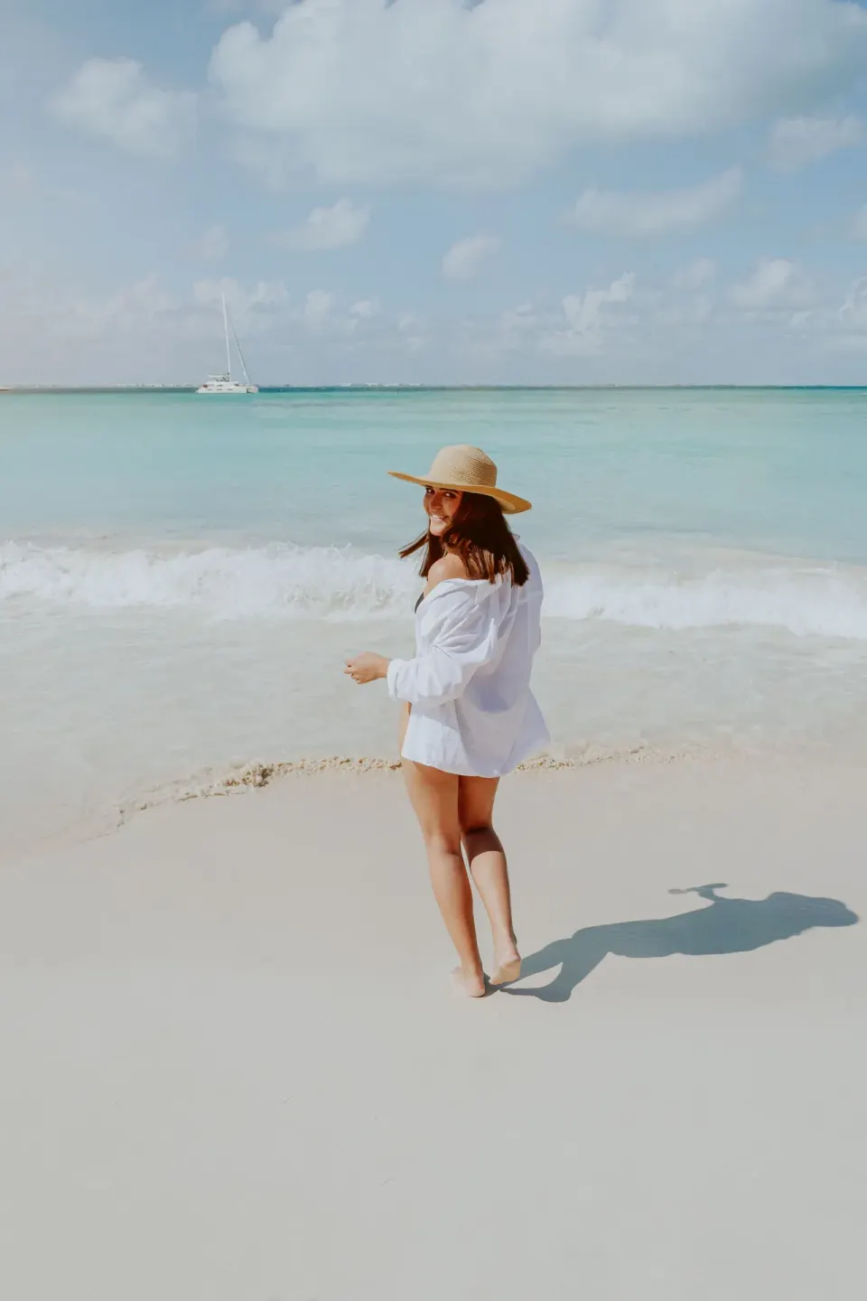A woman in a sun hat walks along the shoreline at Ixchel Beach Hotel.