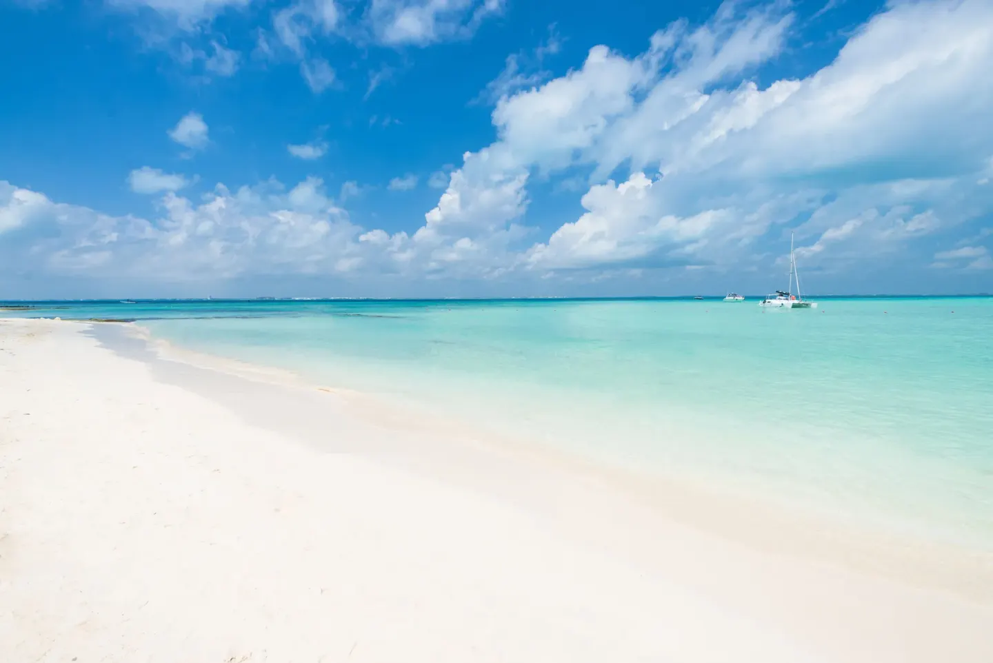 White sand beach and turquoise water by Ixchel Beach Hotel with boats offshore.