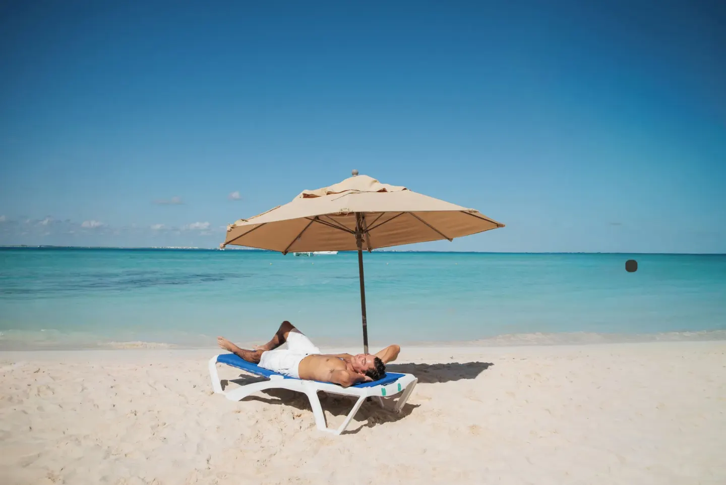 Man relaxes on a beach lounger beneath an umbrella at Ixchel Beach Hotel.