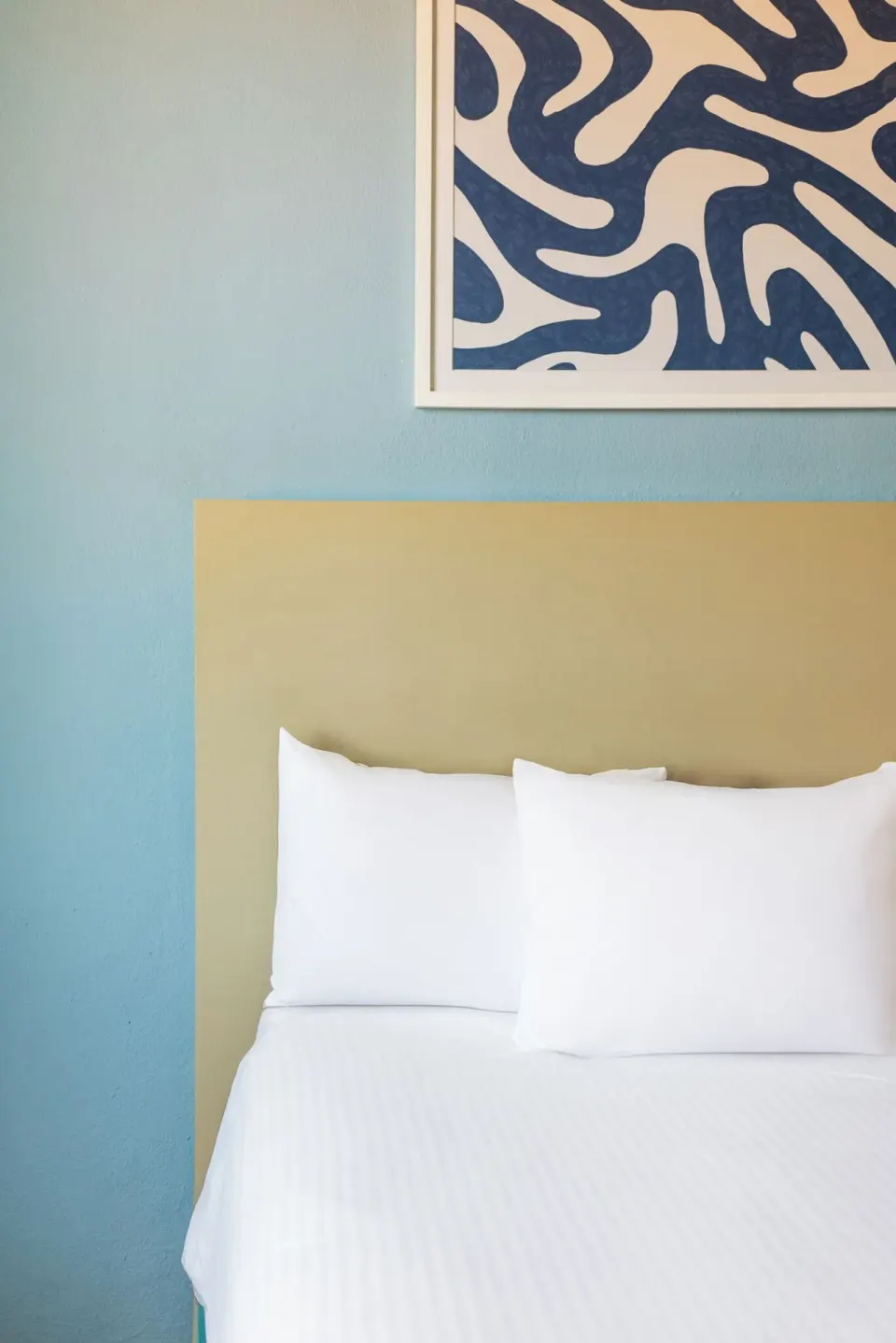 Corner of a Standard Room bed beneath blue wall art at Ixchel Beach Hotel.