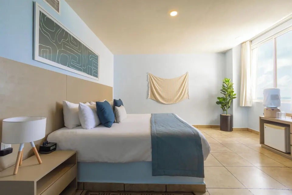 Standard Room at Ixchel Beach Hotel with one bed, large window, and mini fridge area.