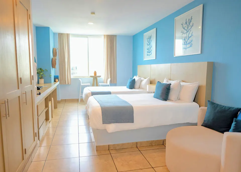 Standard Room at Ixchel Beach Hotel with two beds, seating, desk, and window light.
