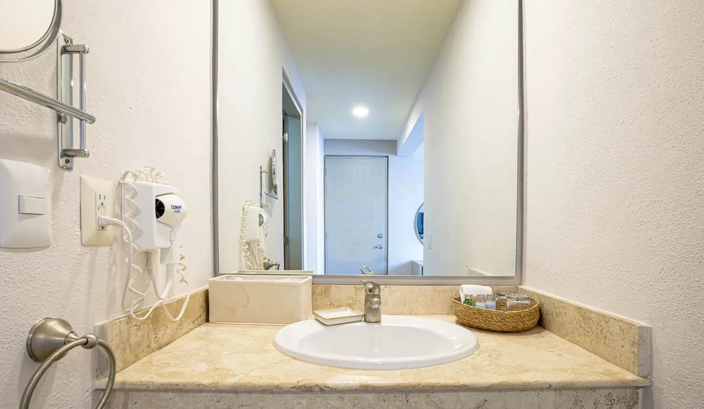 Standard Room vanity with sink, mirror, hair dryer, and amenities at Ixchel Beach Hotel.