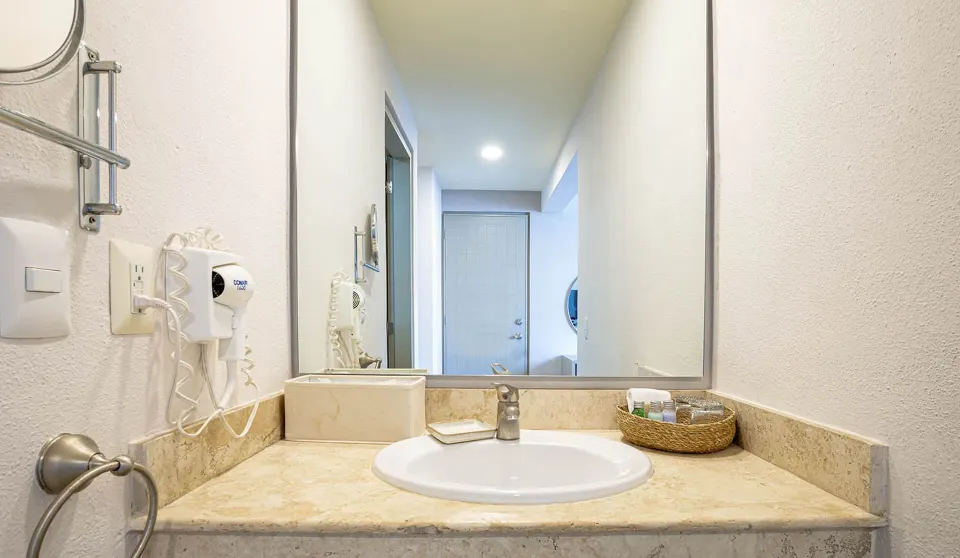 Standard Room vanity with sink, mirror, hair dryer, and amenities at Ixchel Beach Hotel.