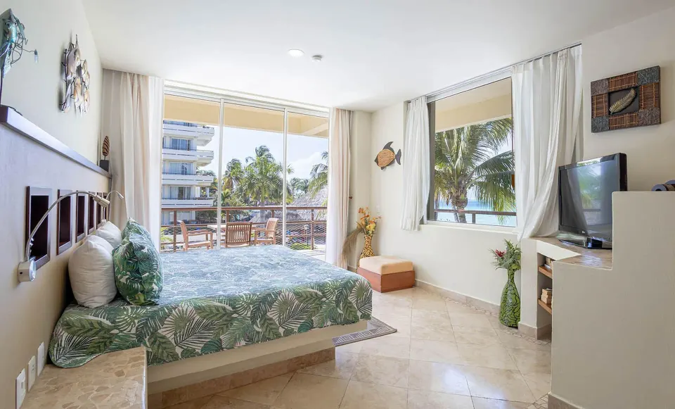 King bedroom with balcony doors and palm views in a beachfront suite at Ixchel Beach Hotel.