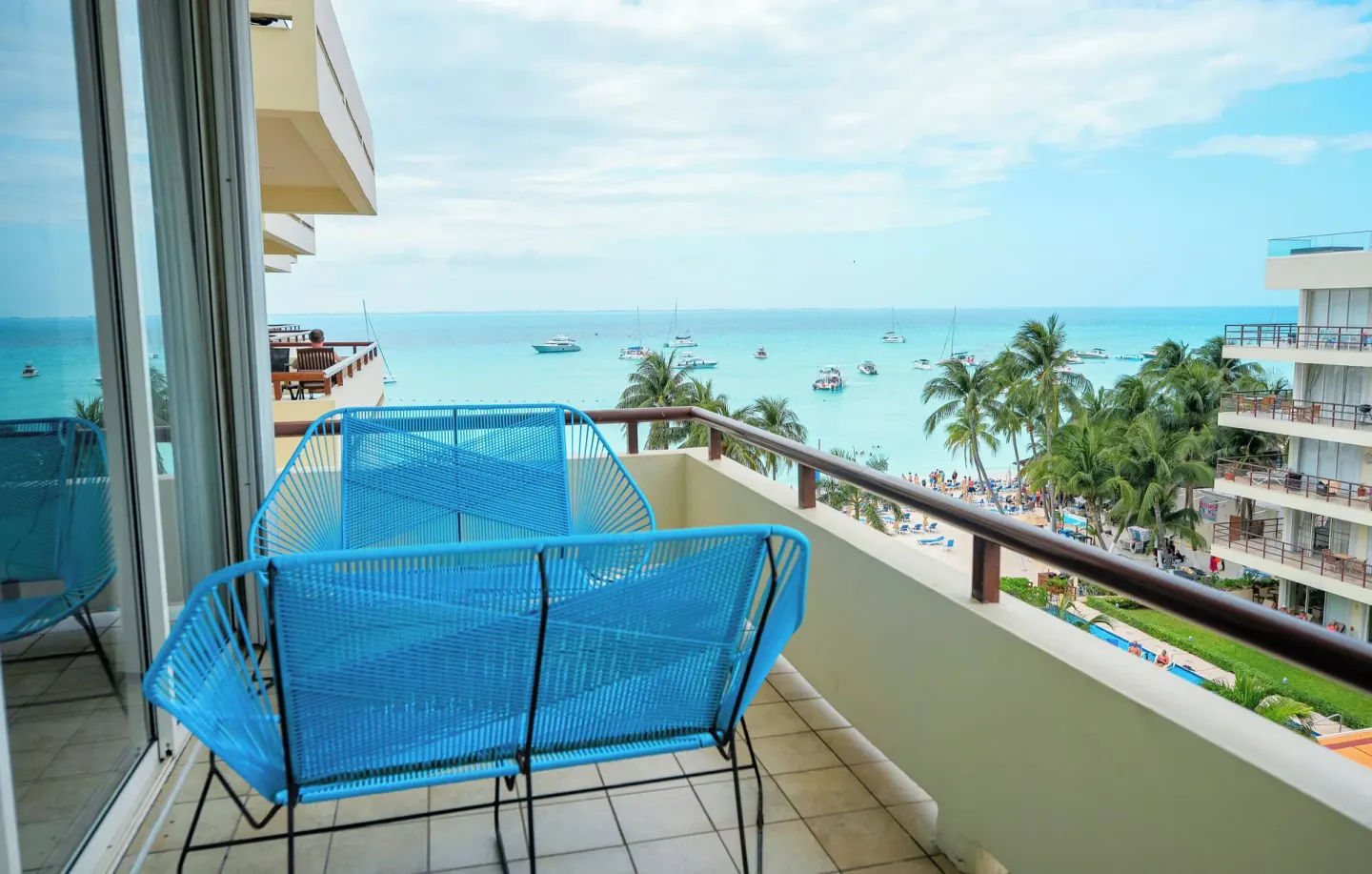 Balcony of a one-bedroom suite at Ixchel Beach Hotel with blue chairs overlooking the beach and sea.