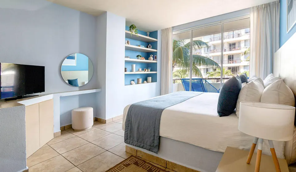 One-bedroom suite at Ixchel Beach Hotel with a king bed, TV, shelves and balcony doors.