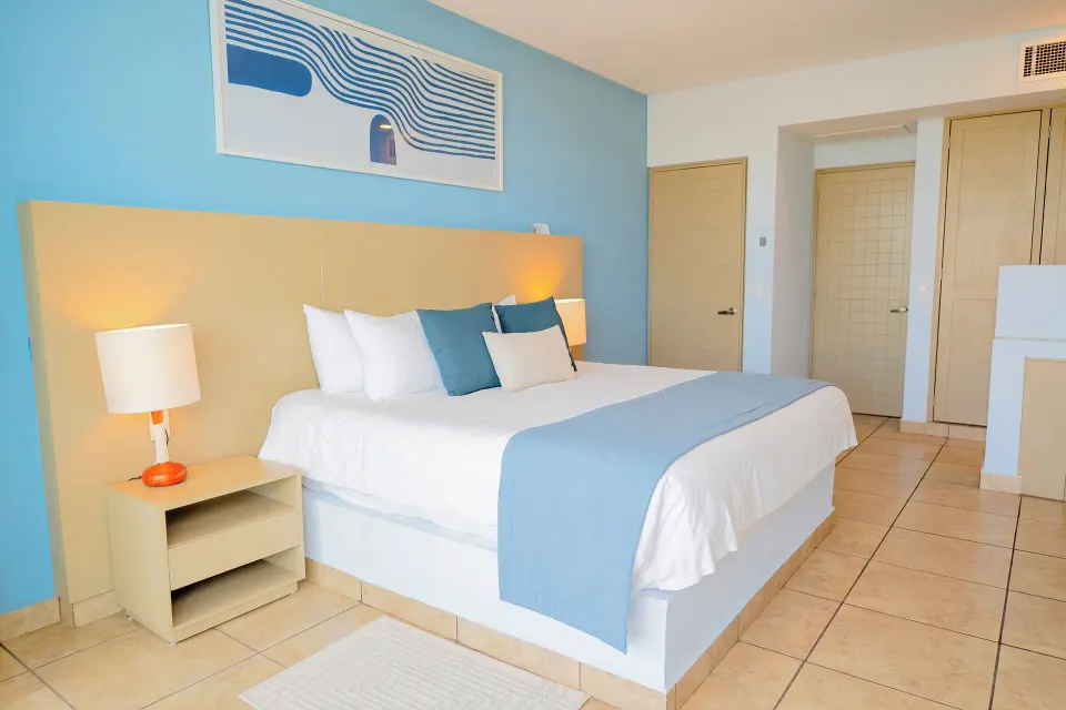 One-bedroom suite at Ixchel Beach Hotel with a king bed, blue accent wall and bedside lamp.