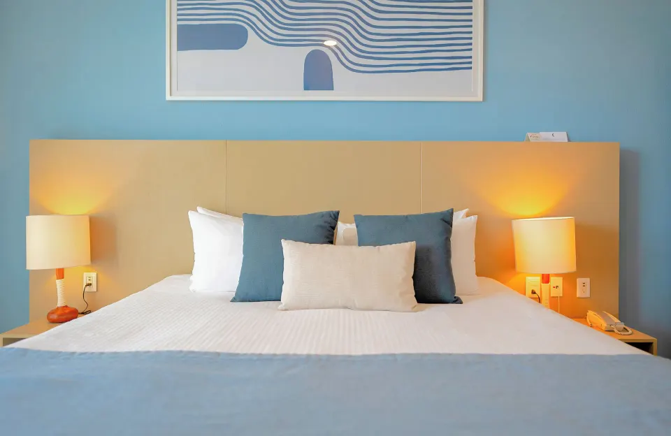 King bed in a one-bedroom suite at Ixchel Beach Hotel with lamps, blue pillows and wall art.