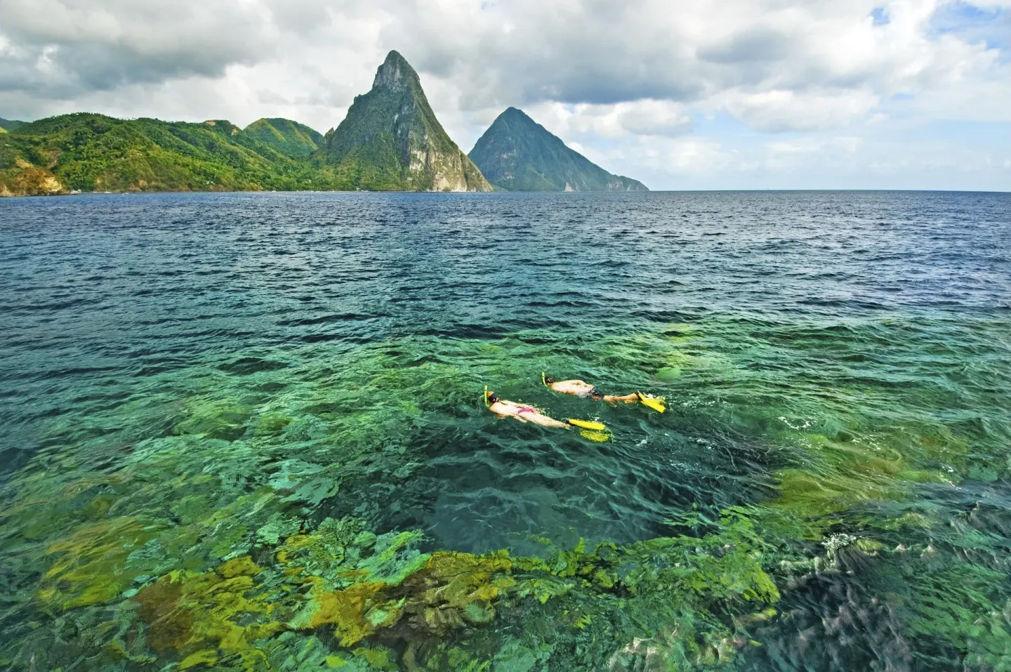 Two snorkelers swim in clear water with the Pitons beyond Jade Mountain Resort.