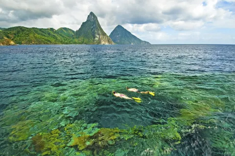 Two snorkelers swim in clear water with the Pitons beyond Jade Mountain Resort.
