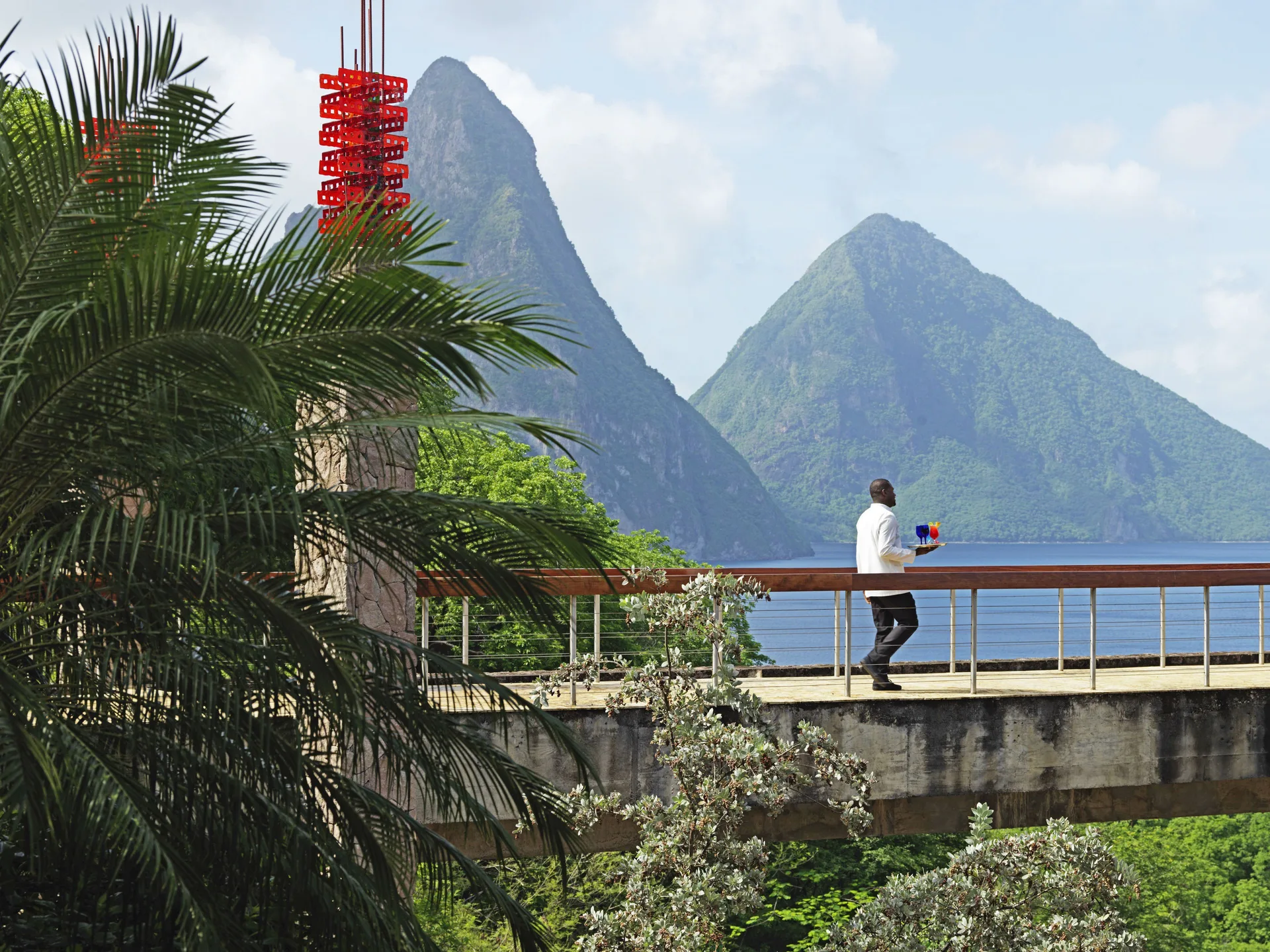 Server carrying drinks along a walkway with the Pitons behind at Jade Mountain Resort.