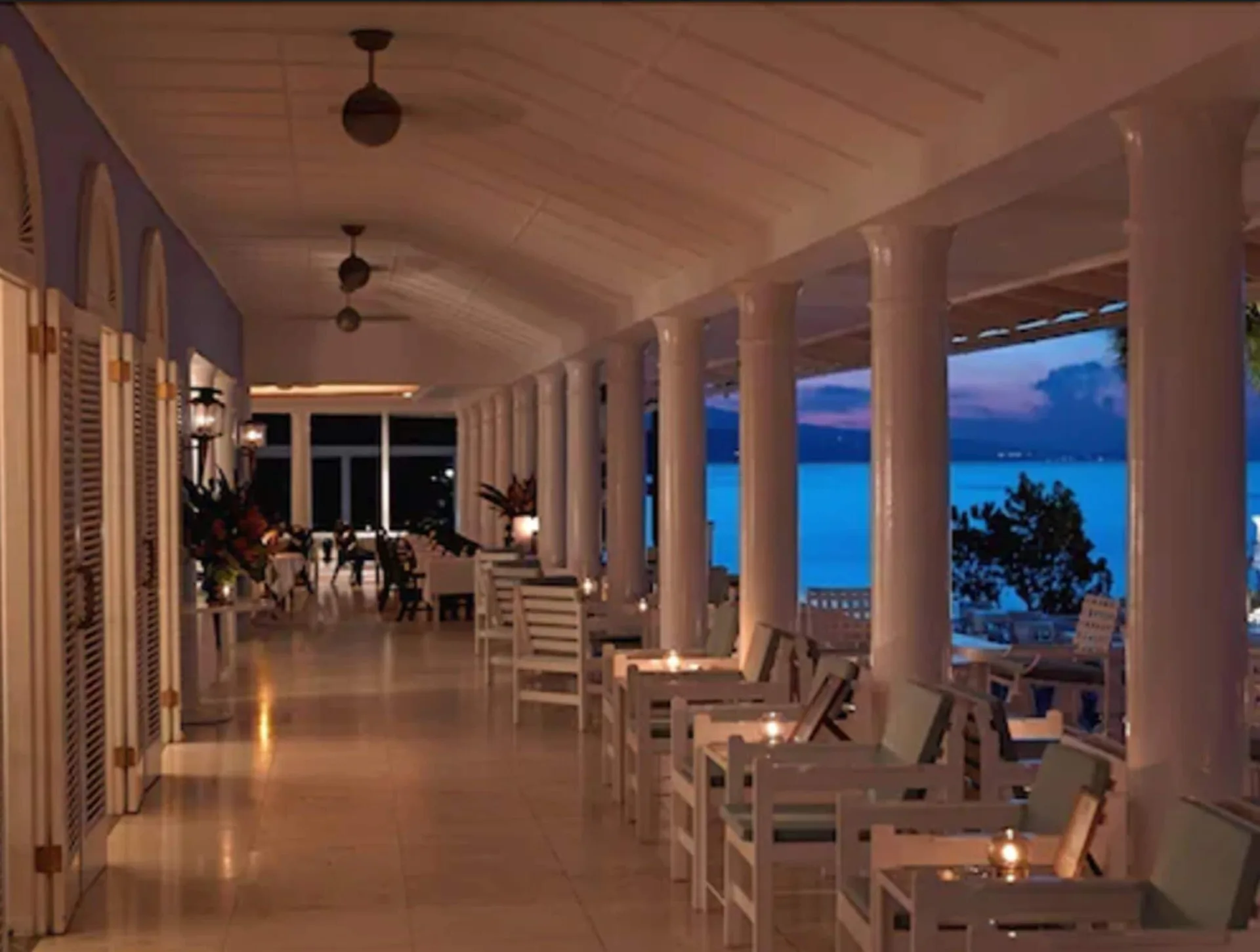 Evening veranda with white lounge chairs, candlelit tables, and sea views at Jamaica Inn.