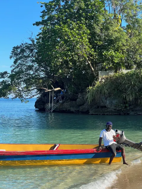 A man sits on a colorful boat at the shoreline near Jamaica Inn.