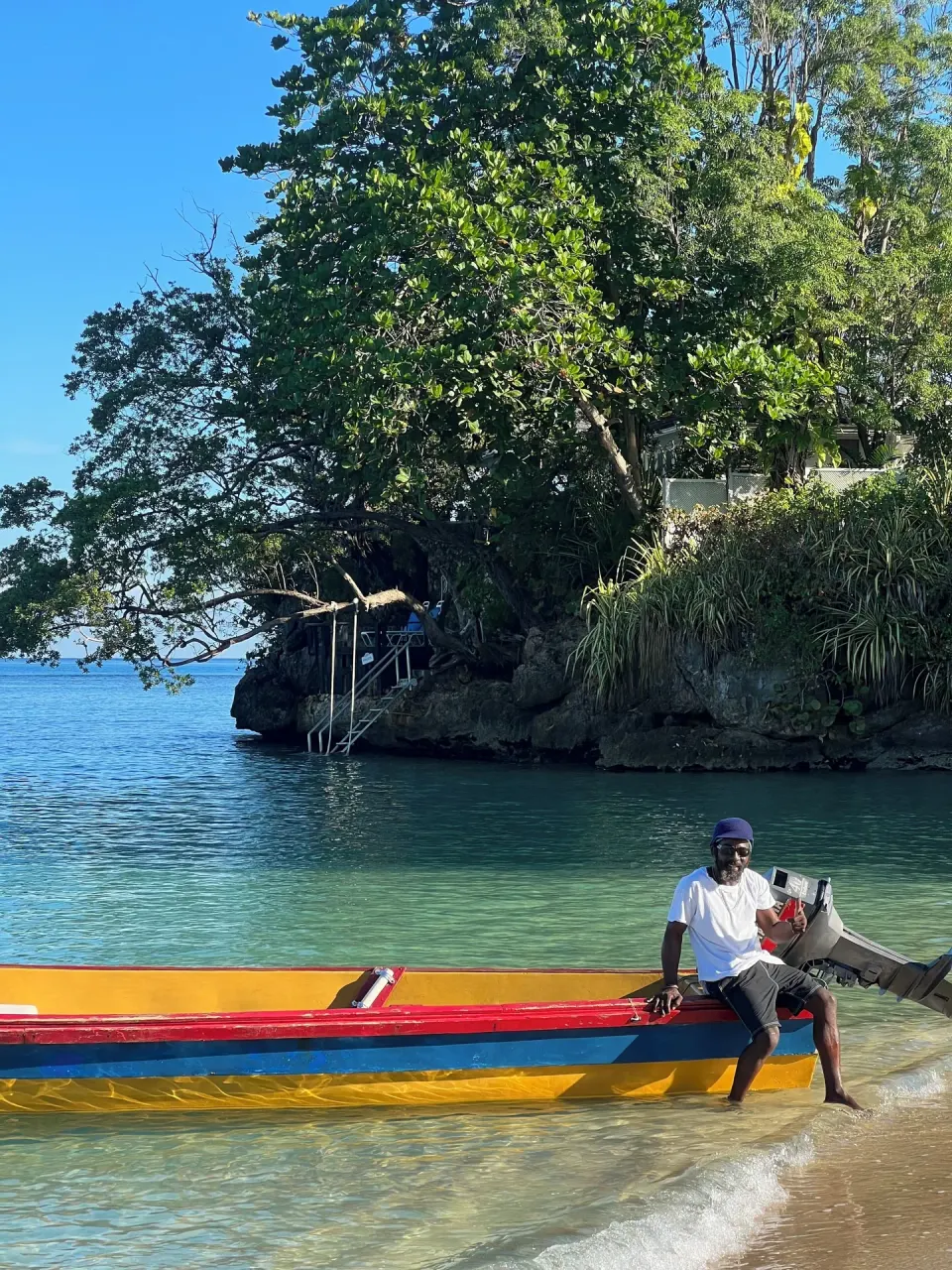 A man sits on a colorful boat at the shoreline near Jamaica Inn.