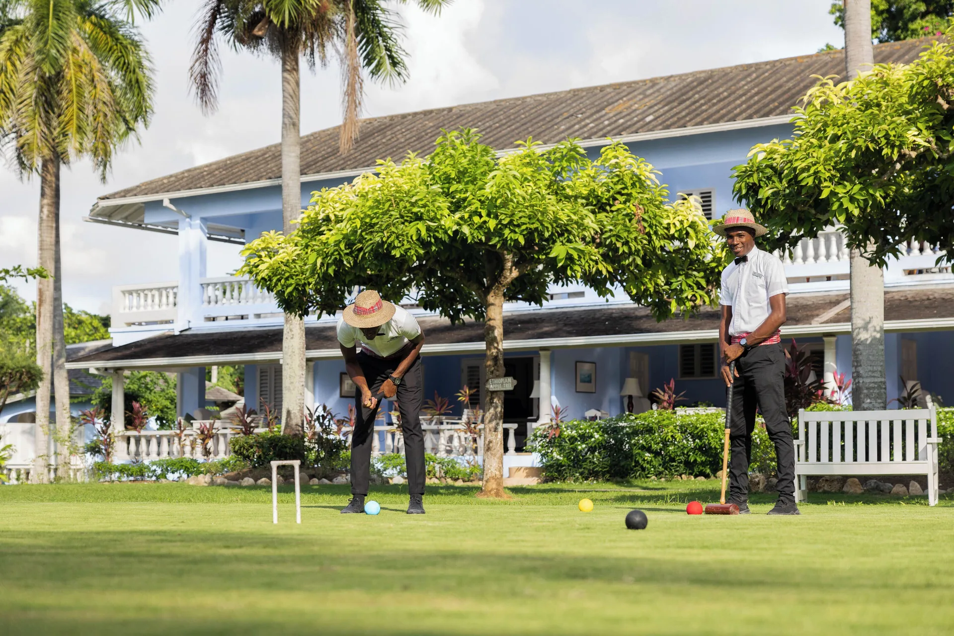 Two people play croquet on a lawn in front of a blue building at Jamaica Inn.