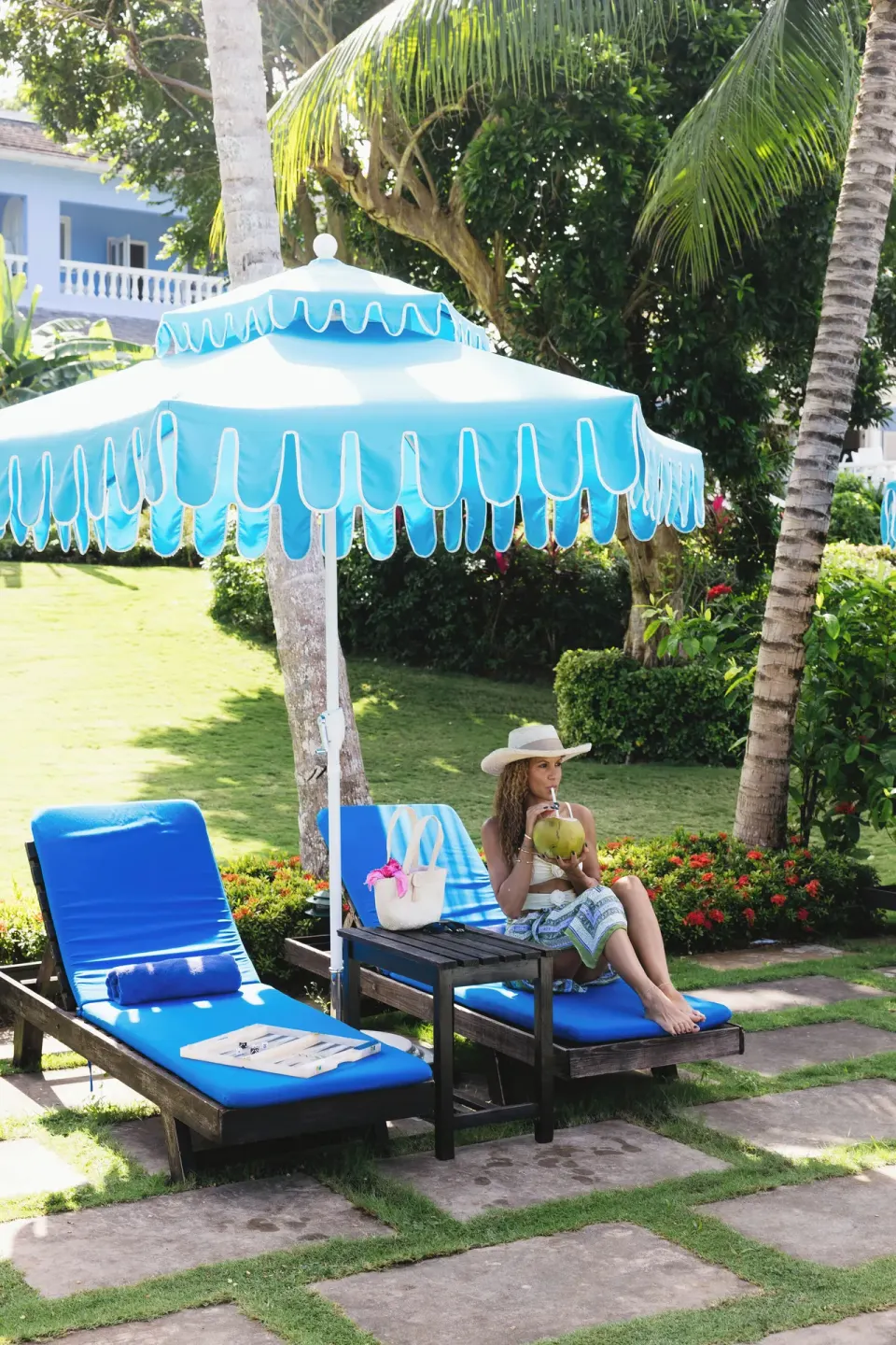 Blue-cushioned loungers under a turquoise umbrella on the lawn at Jamaica Inn.