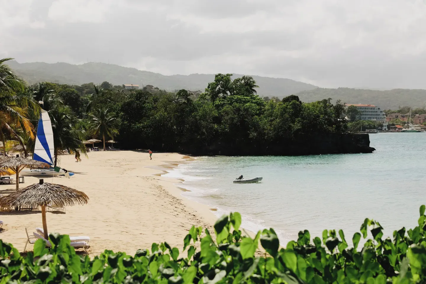 Sandy beach with thatched umbrellas and a sailboat at Jamaica Inn.