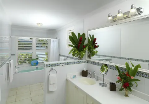 White bathroom with vanity, bathtub, flowers, and louvered ocean-facing windows at Jamaica Inn.