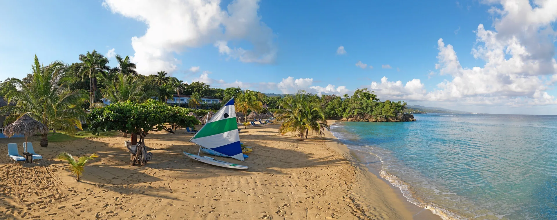 A wide beach view shows a sailboat, palms, loungers, and blue water at Jamaica Inn.