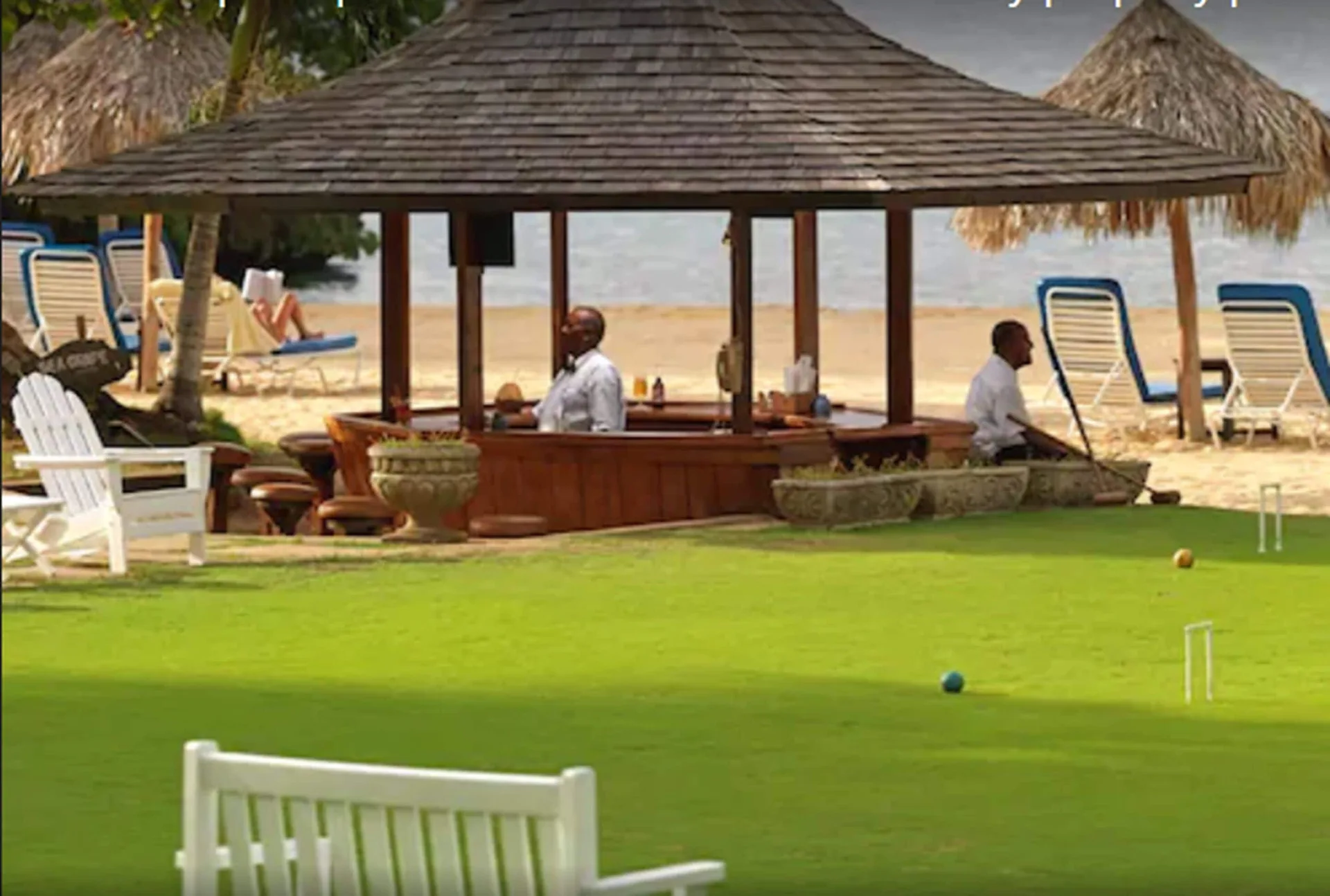 Open-air beach bar pavilion beside a croquet lawn and loungers at Jamaica Inn.
