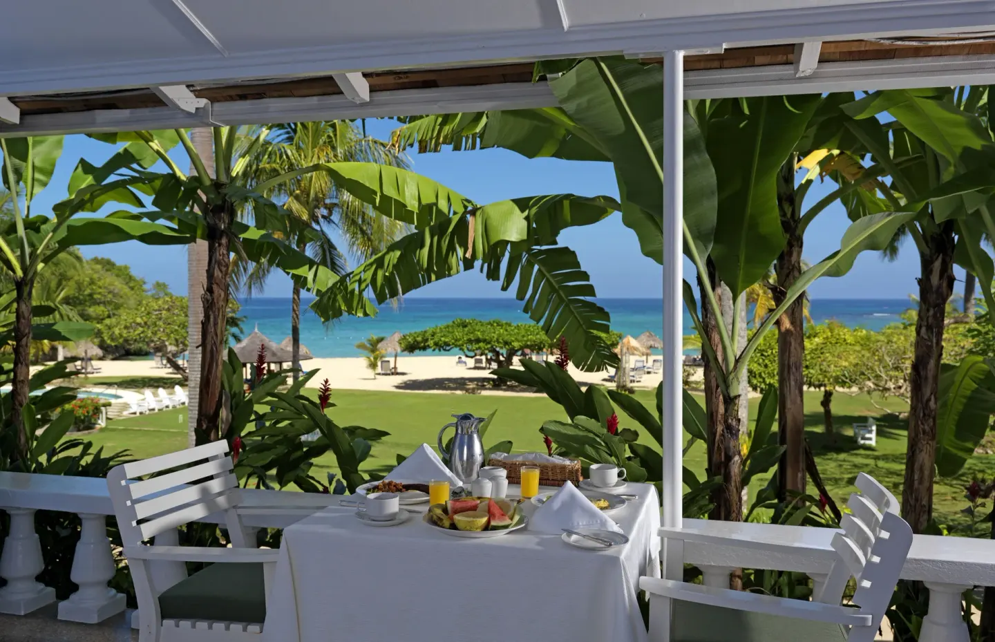 Deluxe Suite verandah dining table framed by palms and ocean at Jamaica Inn.