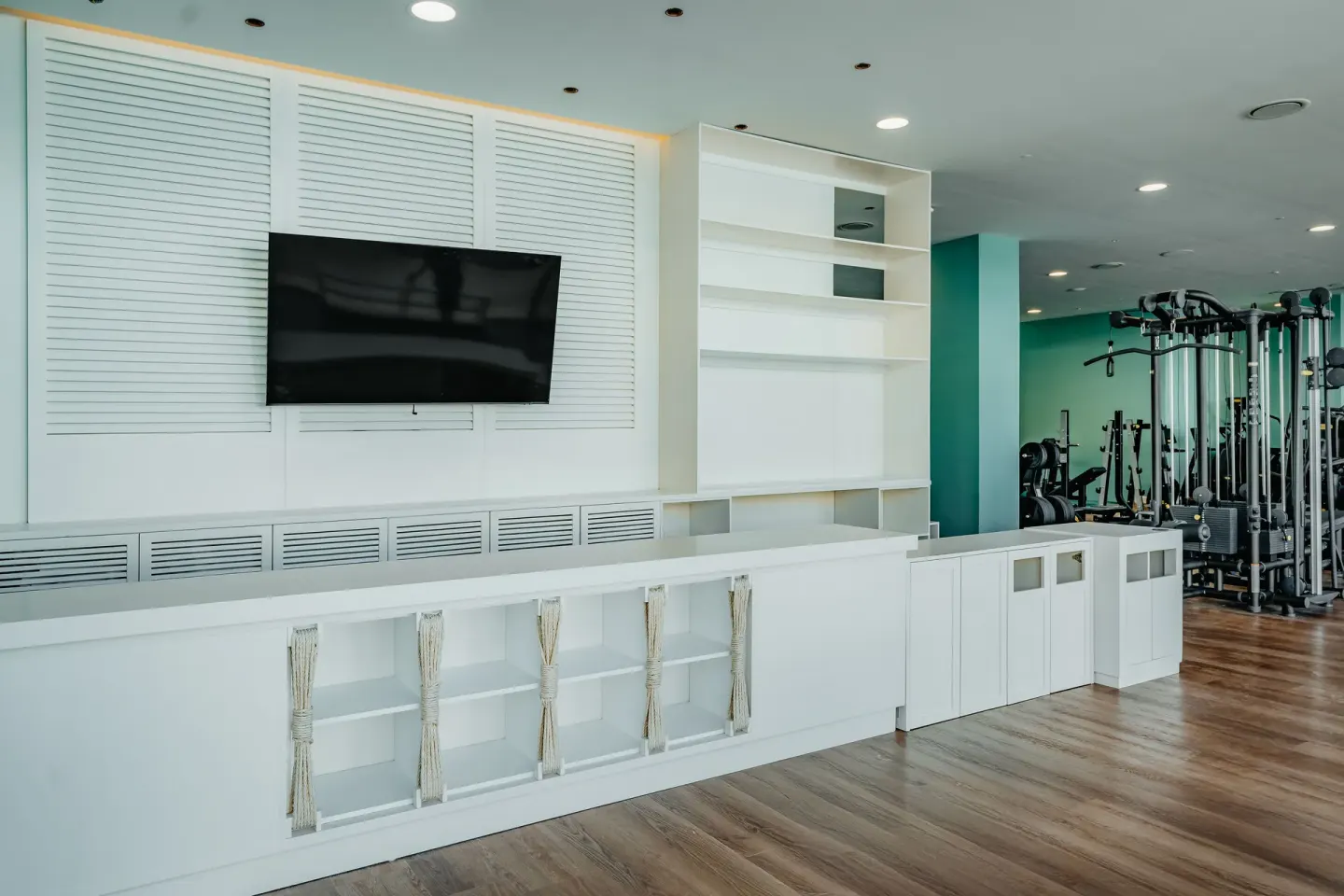 Fitness studio wall with TV, storage shelving and strength machines at JOIA Aruba.