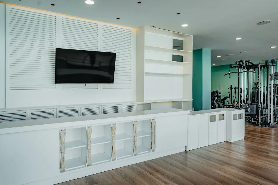 Fitness studio wall with TV, storage shelving and strength machines at JOIA Aruba.