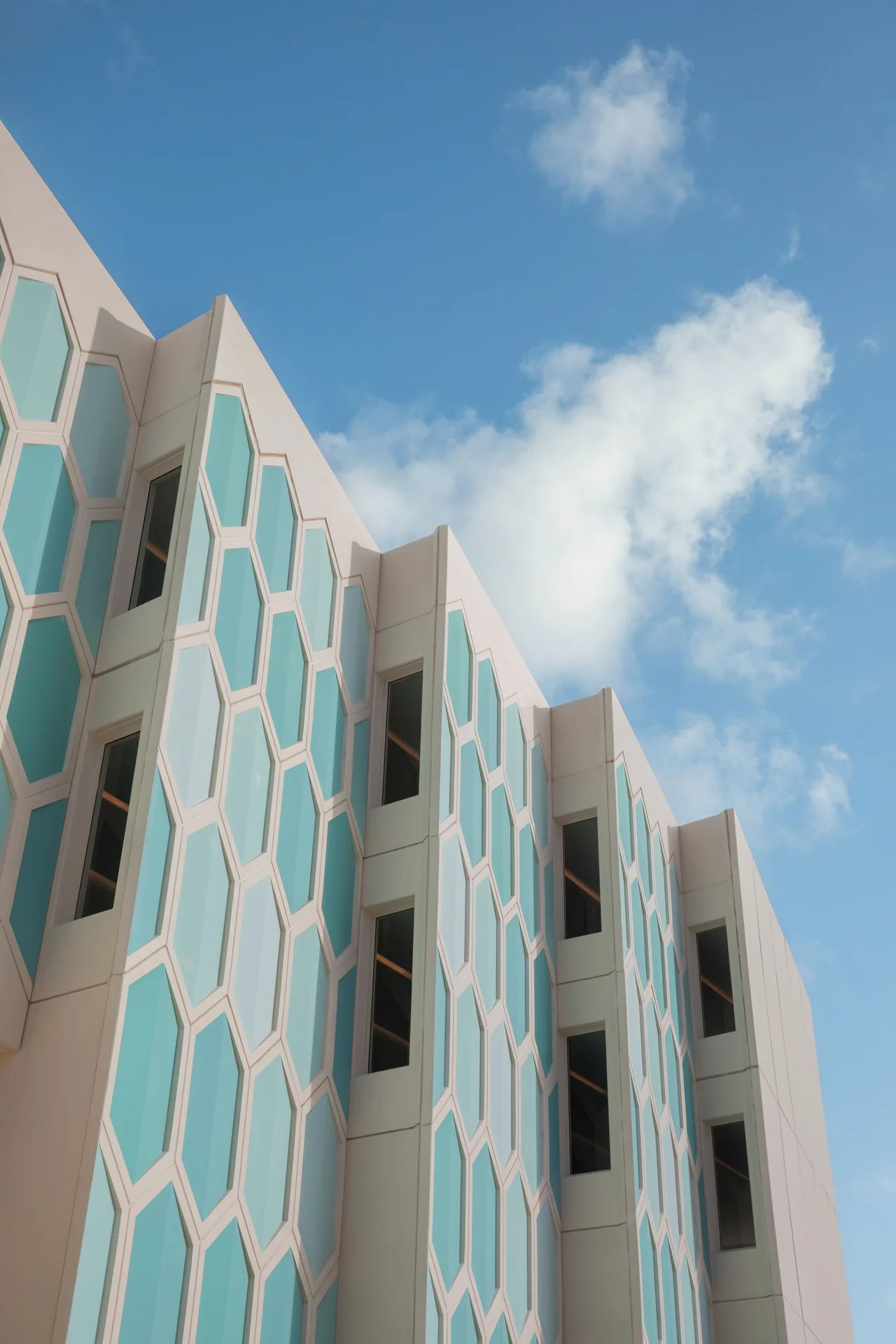 The exterior facade of JOIA Aruba rises against a blue sky with teal geometric panels.