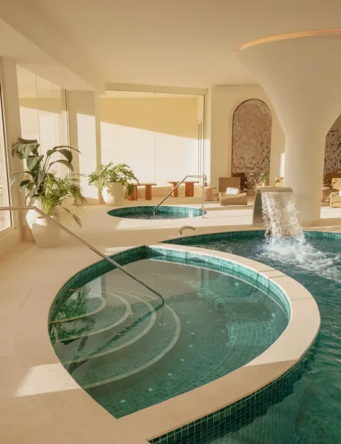 Indoor spa pool with tiled soaking areas and waterfall feature at JOIA Aruba.