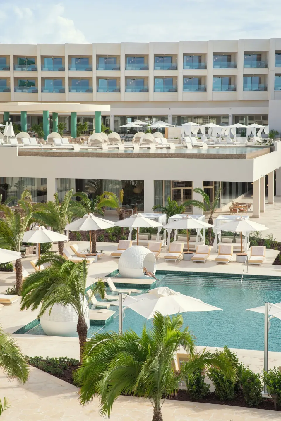 Palm-lined pool deck with umbrellas, cabanas, and balconies at JOIA Aruba.